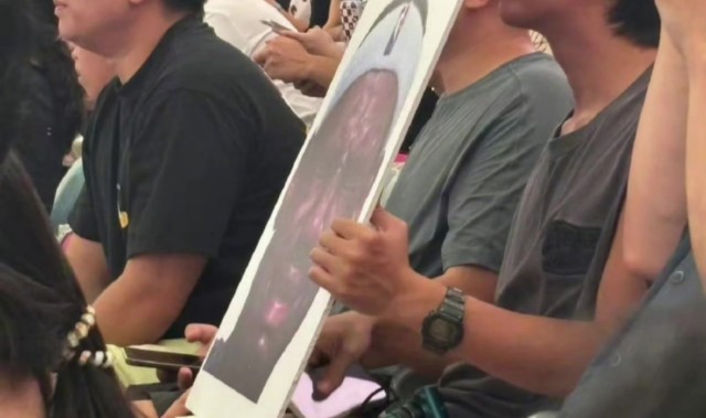 开云登录-詹姆斯中国行成都活动现场 一球迷拿着詹姆斯经典哭脸照坐在场边